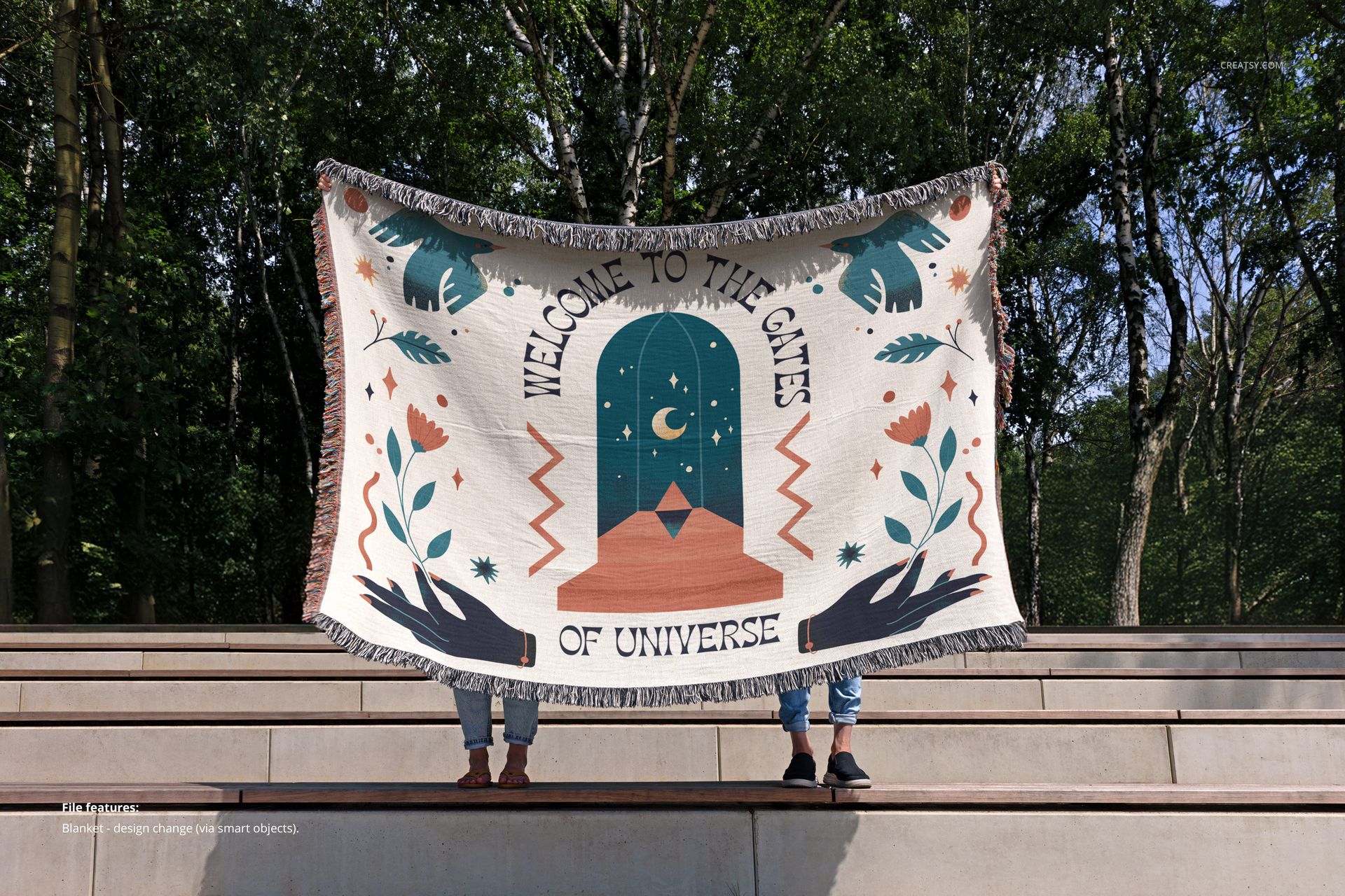 Front view of a jacquard fringed throw blanket mockup, featuring an illustrated pattern, held up by two people outside.