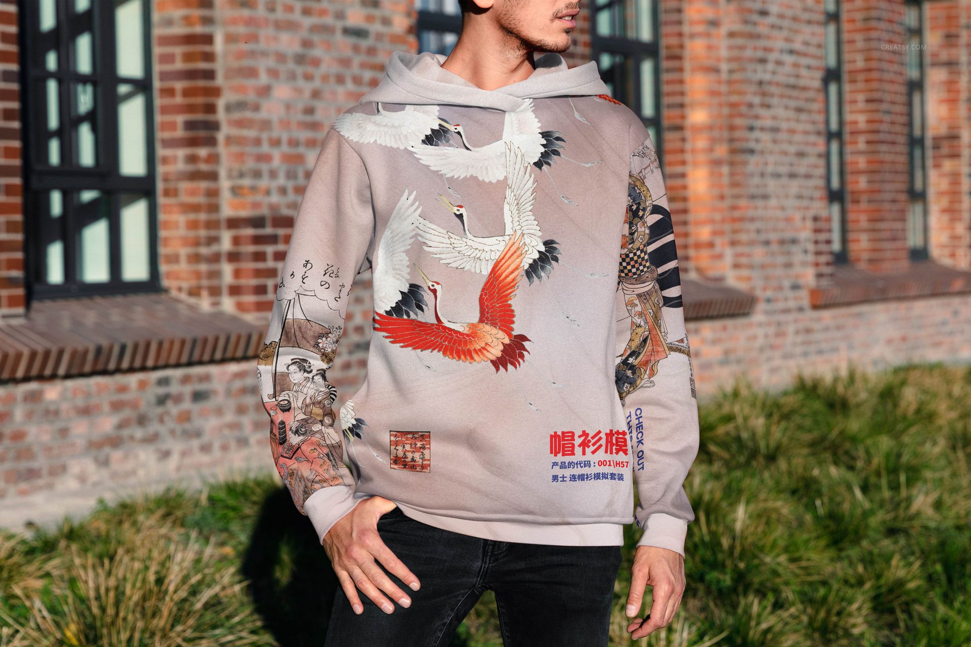 Adult-sized hoodie mockup with colorful crane illustrations and mixed graphics, modeled outdoors near a brick building.