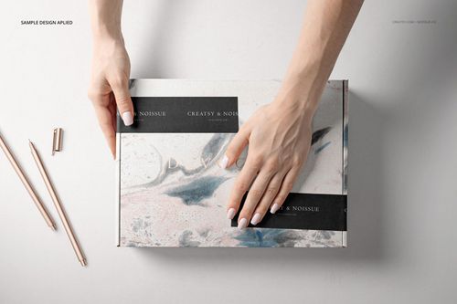 Rectangular packaging box mockup with abstract marble design, black strips, and hands arranging it on a white background.