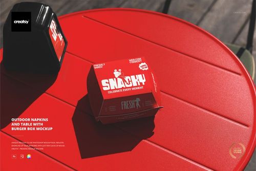 PSD mockup featuring a red burger box and napkin dispenser placed on a circular red table in an outdoor setting.