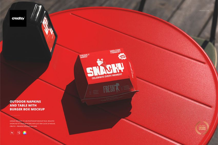 PSD mockup featuring a red burger box and napkin dispenser placed on a circular red table in an outdoor setting.