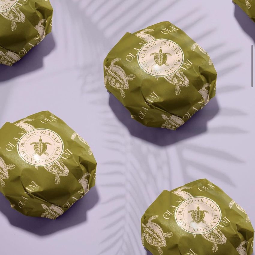 Burger mockup featuring several wrapped burgers in olive green paper with circular cream-colored logos, arranged on a light purple surface.