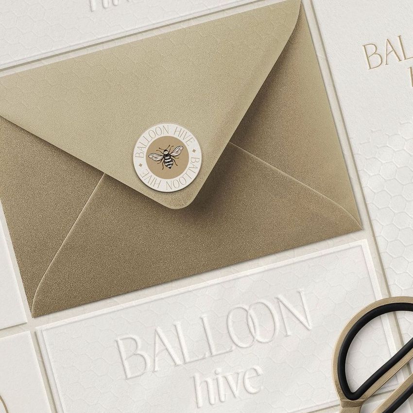 Metallic envelope and card mockup featuring a gold envelope with a bee sticker, surrounded by embossed cards and scissors.