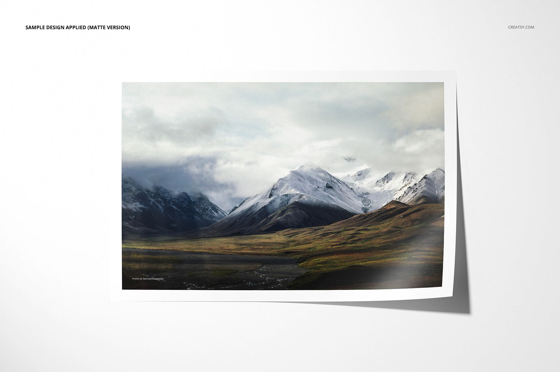 Matte photo print mockup featuring a landscape image of snowy mountains and green hills on a white background.