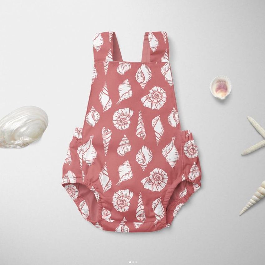 Baby romper mockup with a pink background and white shell patterns, displayed flat on a light surface with seashell props.