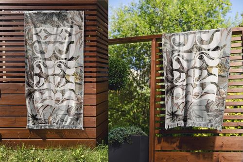 Mockup of a fringed beach towel featuring a swirling gray and white design displayed on a wooden fence outside.