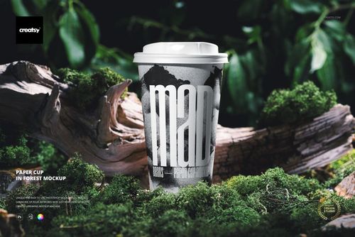 PSD mockup of a paper cup featuring a bold monochrome pattern, placed on green moss among tree branches outdoors.