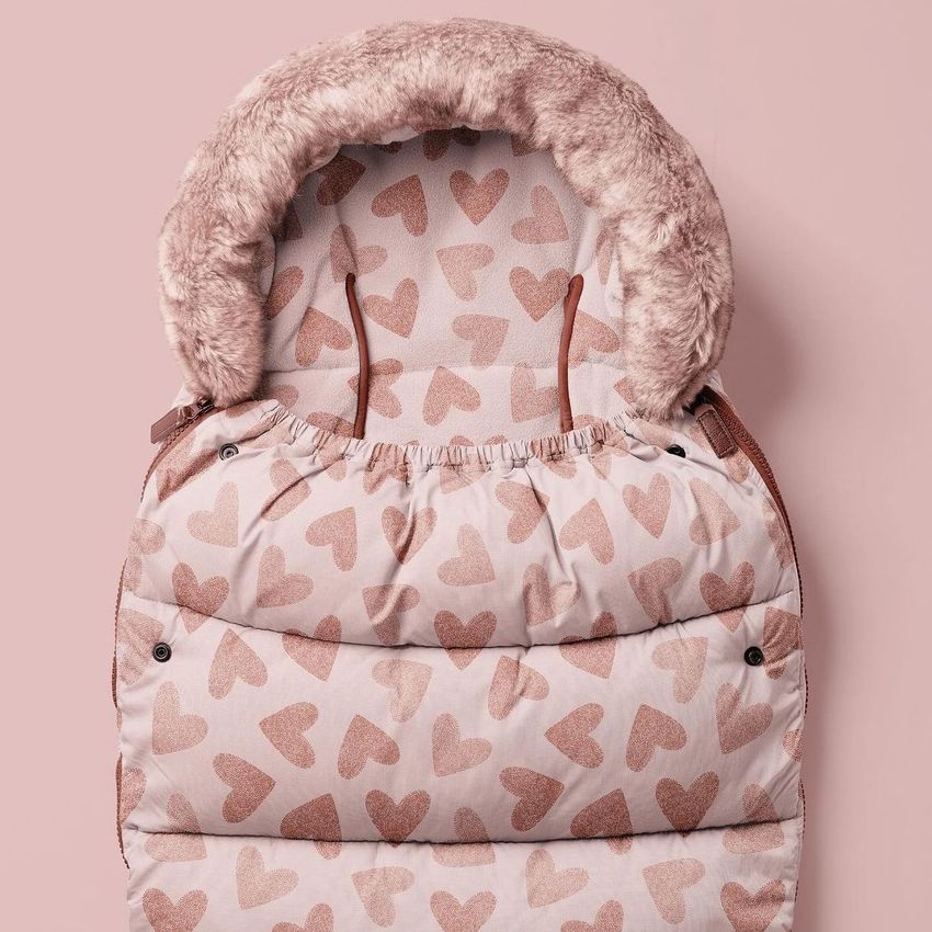 Footmuff mockup featuring a soft pink quilted baby sleeping bag with a fluffy hood and an all-over heart pattern.