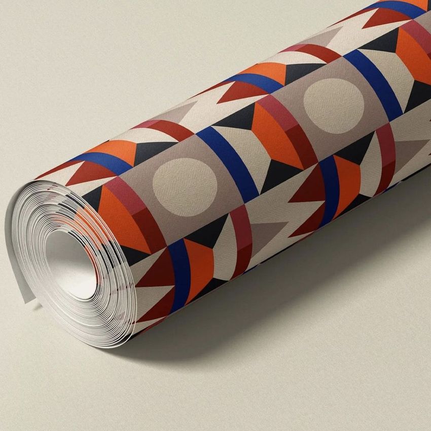 Paper wallpaper mockup featuring a rolled sheet with geometric shapes in red, orange, blue, and beige on a neutral surface.