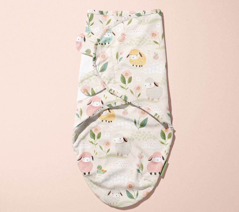 Baby swaddle wrap mockup featuring a pastel sheep and floral pattern, displayed flat on a light pink background.