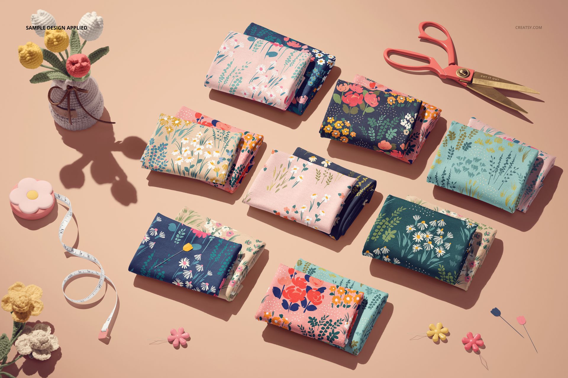 Folded jersey fabric mockup featuring various floral designs, displayed alongside scissors, tape measure, and knitted flowers.