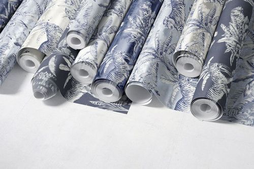 Paper wallpaper mockup showing several patterned rolls with botanical and animal motifs, photographed from above.