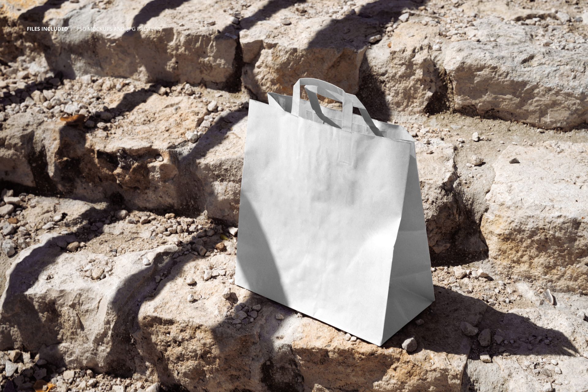 Paper bag mockup featuring a plain white bag with handles set on textured outdoor stone steps in daylight.