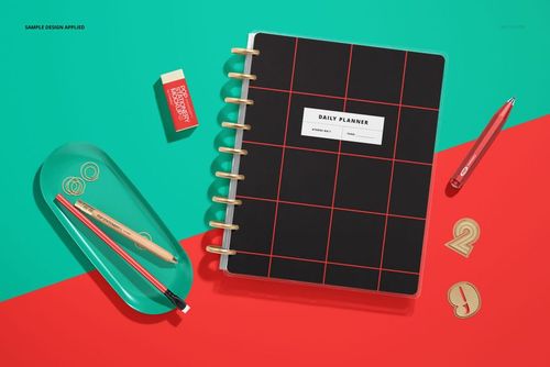 Spiral daily planner mockup with red grid pattern, pencil, pen, eraser, and paper clips arranged on a green and red surface.
