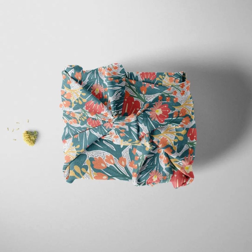 Fabric gift wrap mockup featuring a square package wrapped in floral patterned cloth with green, orange, and white colors.