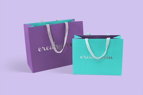 PSD mockup showing a pair of colorful paper shopping bags with silver lettering and white handles on a pastel backdrop.