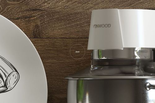 Close-up view of a white plate with a black line drawing next to a stainless steel kitchen appliance on a wooden surface.