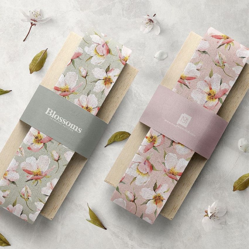 Two cotton ribbon mockups with cherry blossom patterns displayed on wooden paddles, surrounded by petals and leaves on a light stone surface.