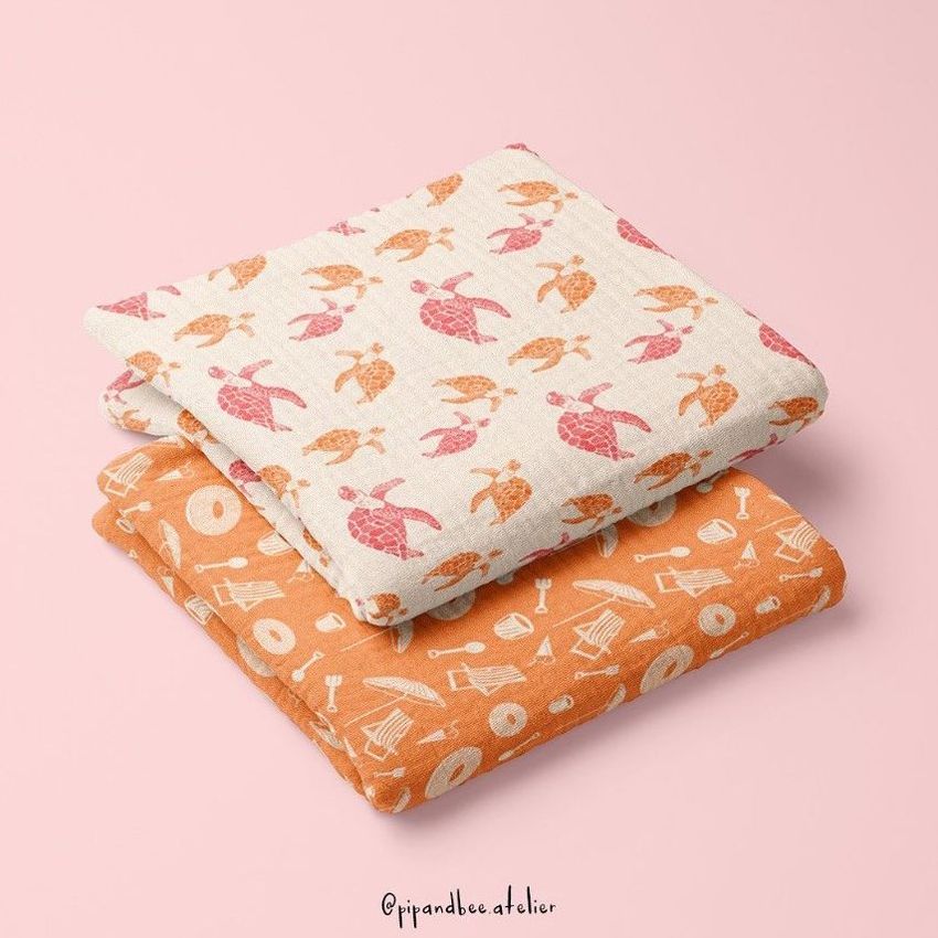 Two crinkle muslin swaddle blankets folded and stacked on a pastel pink surface, featuring turtle and geometric patterns.