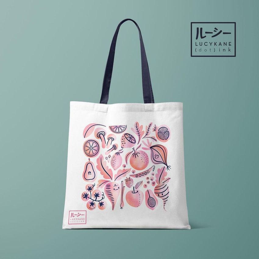 Tote bag mockup featuring a white bag with a colorful hand-drawn vegetables and fruits pattern on the front, set against a muted green background.