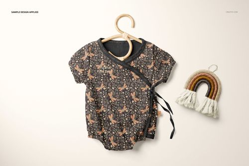 Front view of a short-sleeve muslin onesie mockup with a floral pattern on a wooden hanger, next to a rainbow-shaped decor.