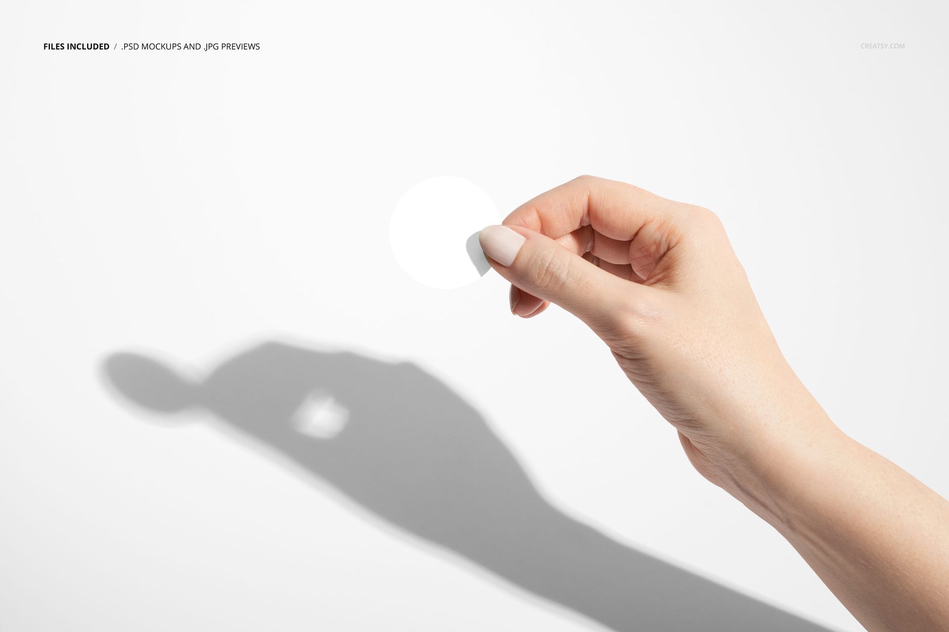 Round sticker mockup held between fingers against a white background, casting a distinct shadow on the surface.