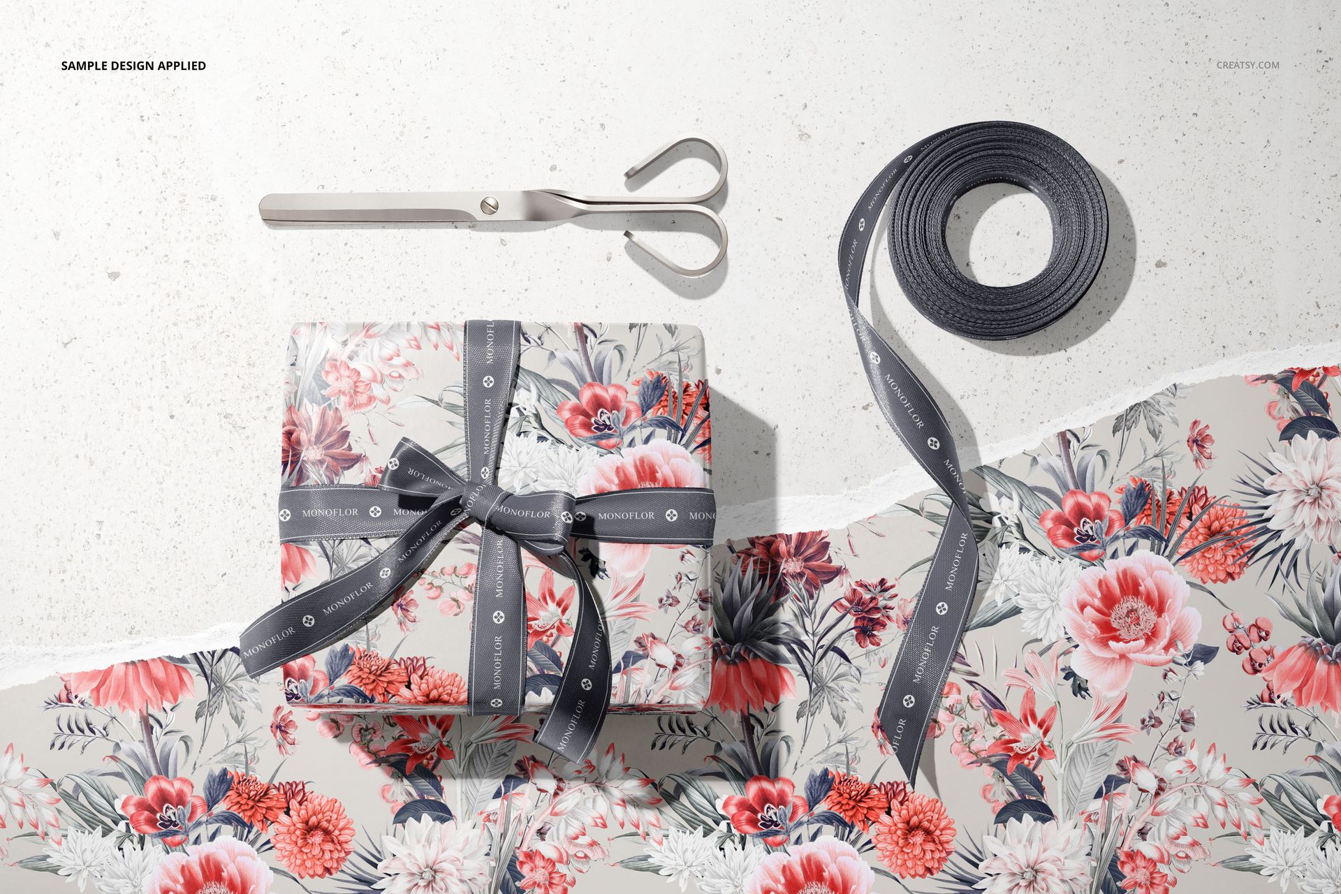 Top view of a mockup featuring a wrapped gift box with floral paper, ribbon, scissors, and unrolled wrapping paper.