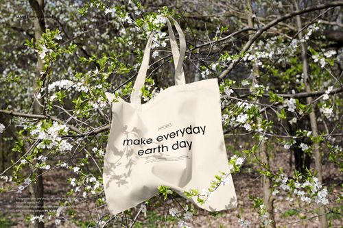 Neutral-colored tote bag mockup displayed on a flowering tree branch, surrounded by white blossoms and greenery.