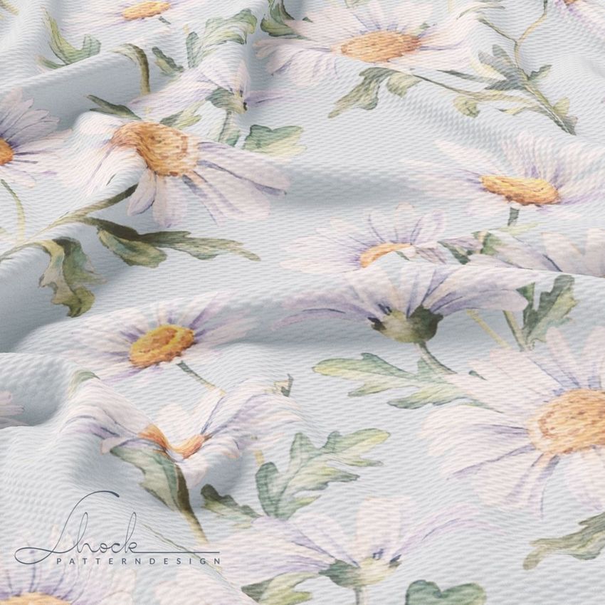 Bullet fabric mockup featuring a soft blue textile with a repeating pattern of white daisies and green leaves, shown with gentle folds.