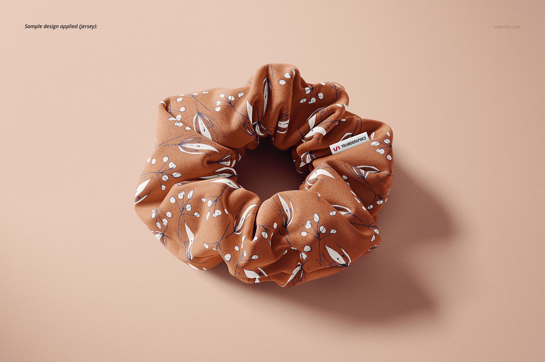 Brown hair scrunchie with white leaf and dot pattern displayed on a light beige surface in a top view mockup.