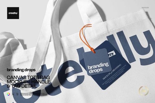 Detailed PSD mockup of a canvas tote bag featuring bold blue lettering, white fabric, and a branded tag with orange string.