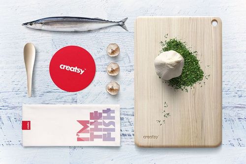 Top view of seafood restaurant mockup set with fish, wooden cutting board, herbs, shells, spoon, and napkin on white surface.