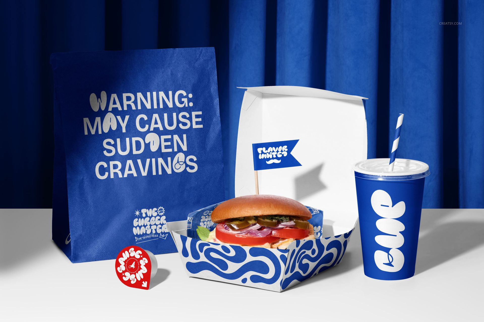 Front view of vegan burger packaging mockup with blue and white branding, cup, box, and paper bag on a table.