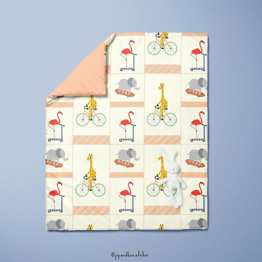 Baby duvet cover mockup featuring a playful animal pattern with giraffes, elephants, and flamingos on scooters and bikes, shown on a flat blue background with a plush bunny toy.