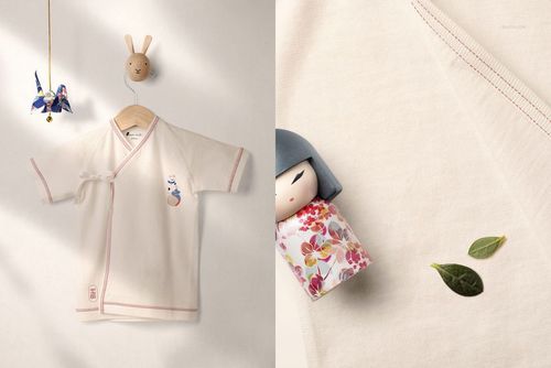 Organic cotton baby kimono bodysuit mockup displayed on a wooden hanger, with soft cream fabric and pink trim.