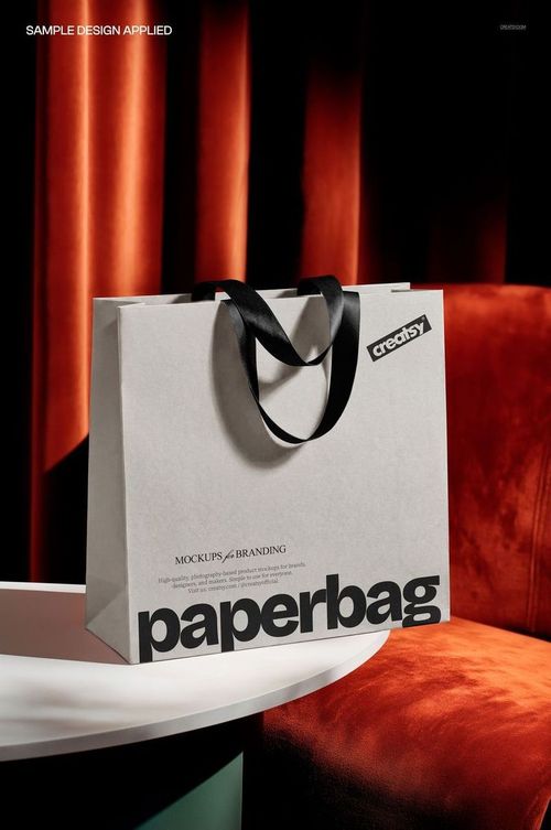 Luxury paper shopping bag mockup featuring black ribbon handles, set against a rich orange and brown velvet backdrop.