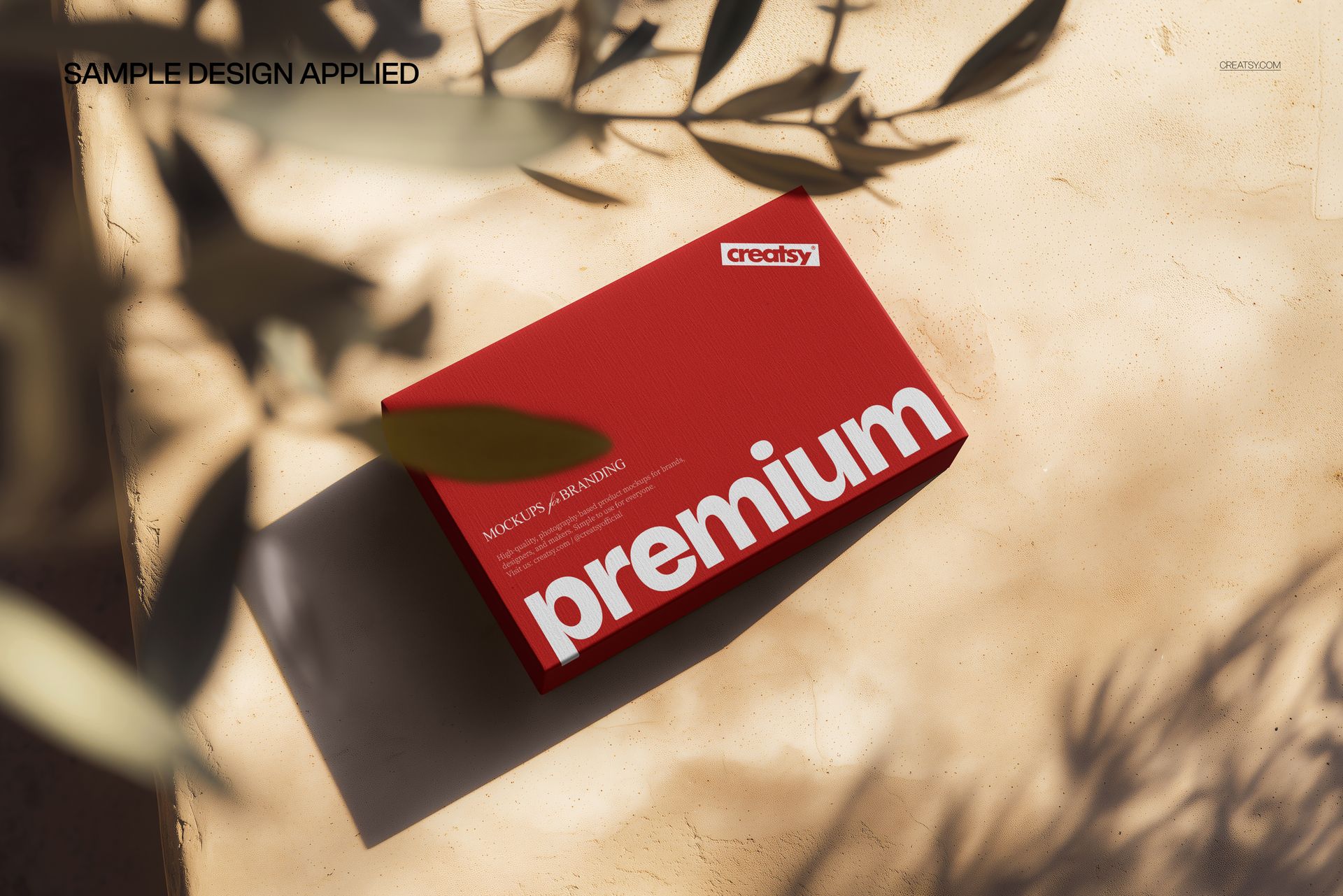 Top view of a red packaging box mockup on a beige stone background with leafy shadows and sunlight.