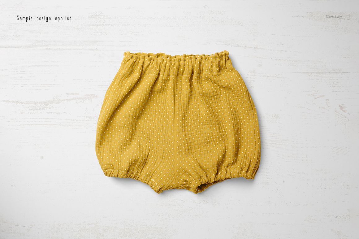 Yellow baby shorts with small white dots, shown from above on a pale textured background in a mockup scene.