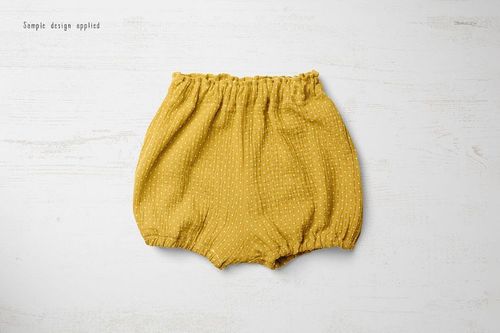 Yellow baby shorts with small white dots, shown from above on a pale textured background in a mockup scene.