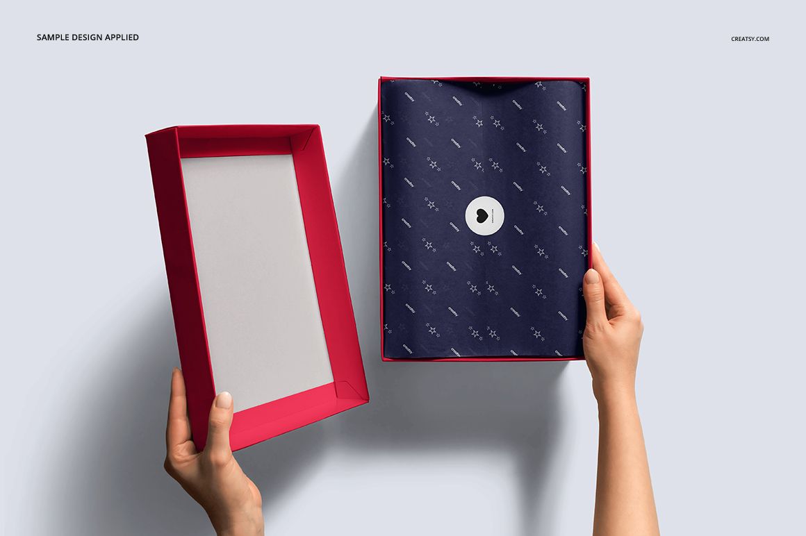 Top view of a shoe box mockup set with a red lid, navy patterned tissue paper, and hands holding the box and lid.