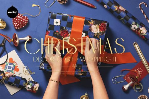 PSD mockup showing hands decorating a blue floral gift box with ribbon, with festive wrapping paper and props nearby.