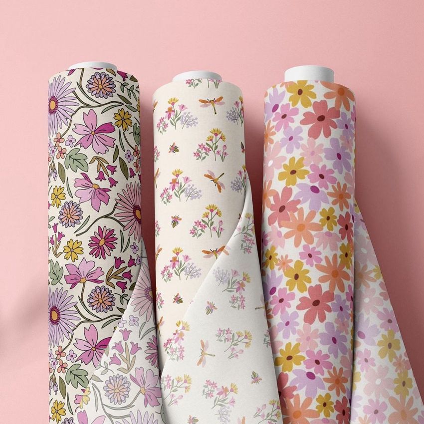 Three fabric rolls mockup featuring floral patterns in pink, yellow, and orange tones, standing upright against a pastel pink background.