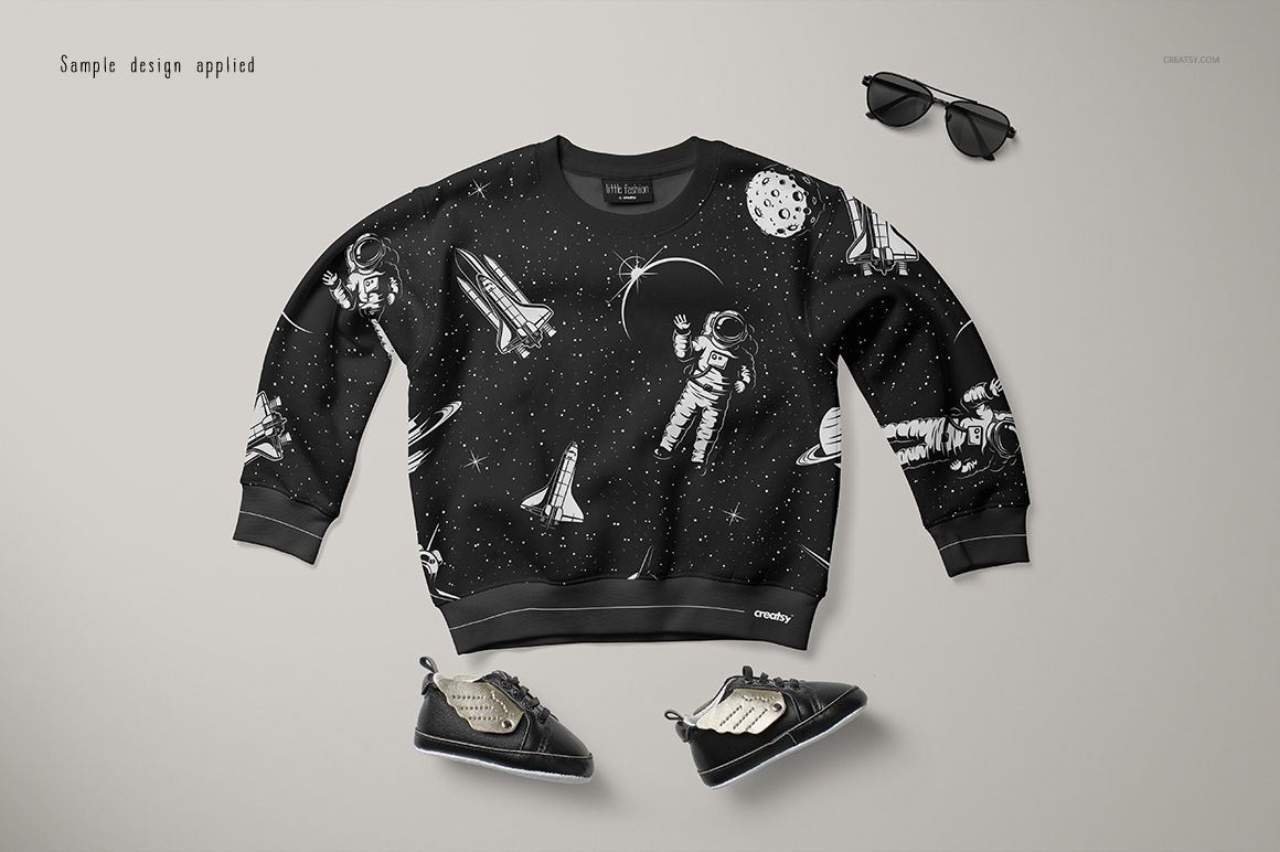 Front view of a baby sweatshirt mockup with a black background and white space-themed illustrations, placed on a light surface.