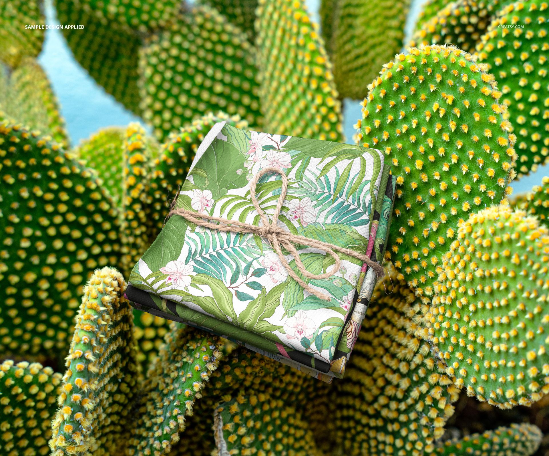PSD mockup showing a bundle of patterned fabric with floral and leaf designs resting on spiky cactus pads.