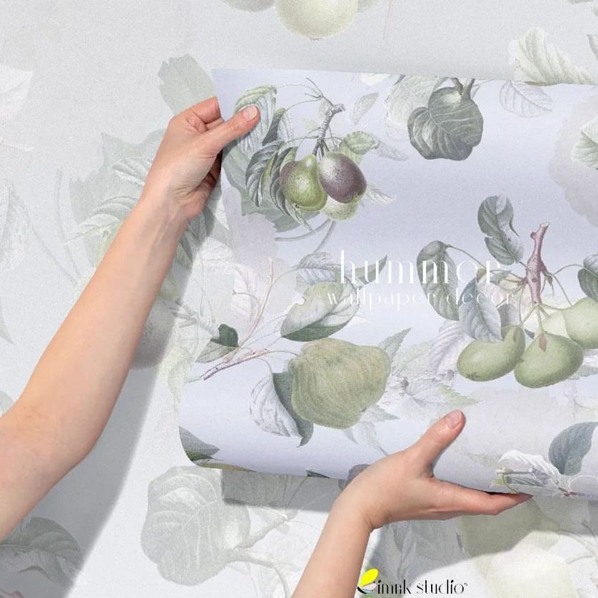 Hands holding a rolled sheet of paper wallpaper mockup with a botanical fruit and leaf pattern against a matching wall.