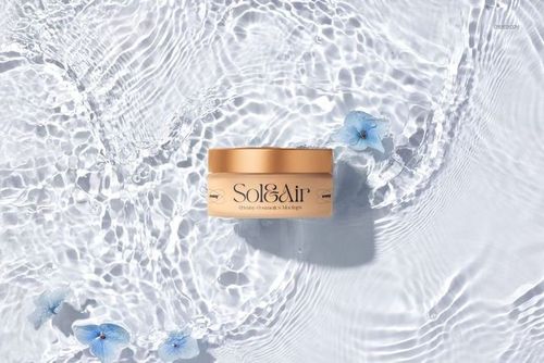 Cosmetics packaging mockup featuring a golden jar on textured water surface with delicate blue flowers, overhead angle.