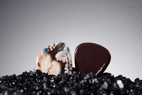 Front view of two guitar picks on textured black stone, one with abstract patterns and one in deep brown, PSD mockup.