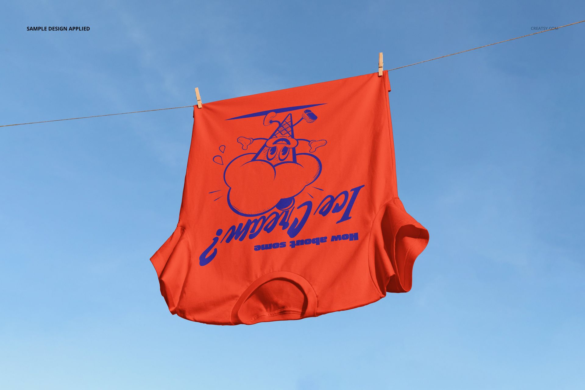 PSD mockup of a red short-sleeve t-shirt with blue print displayed outdoors, clipped to a line with sky background.