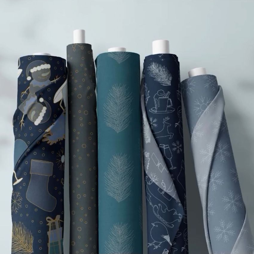 Fabric rolls mockup showing five upright rolls with winter and Christmas-themed patterns in blue, teal, and gray tones.