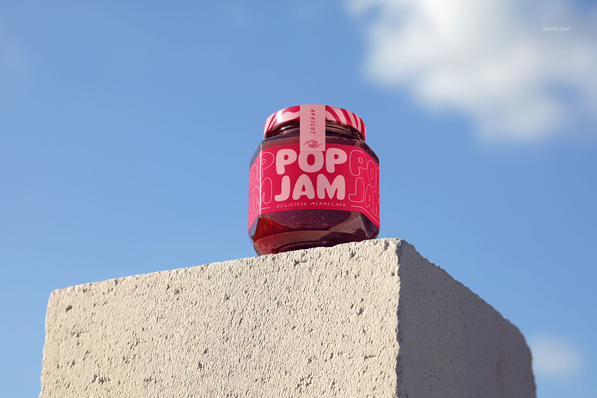 Cherry jam jar mockup with a pink patterned label and lid, shown in front view outdoors on a textured concrete surface.